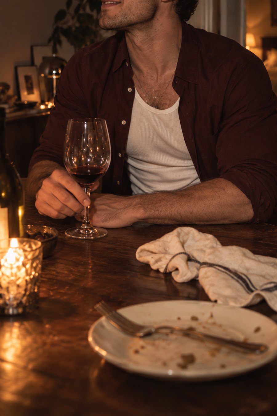 Jude Bellamy at the dinner table, framed from the mouth down, turning the stem of a wine glass